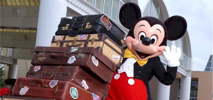 Mickey mouse is standing next to a stack of suitcases.